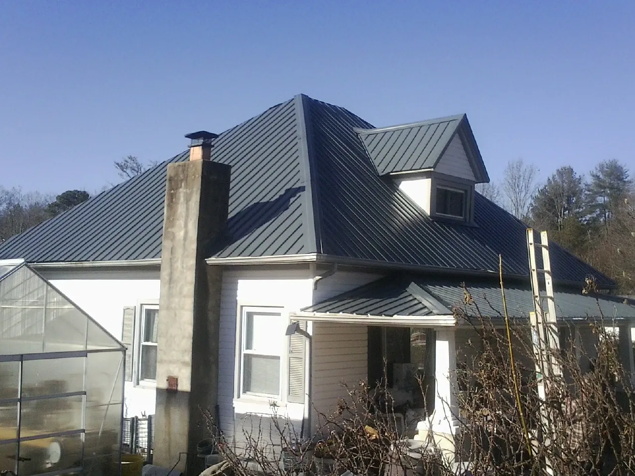 Dark blue standing seam metal roof on a white farmhouse with dormer — Slate & Tile Roof Repair by Roofing Brothers in Kinston
