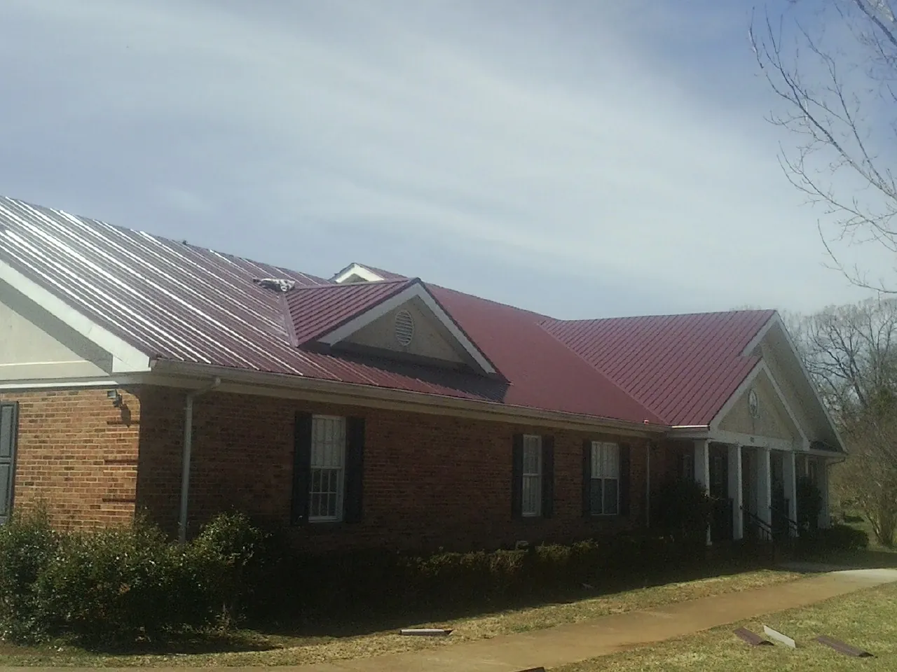 Red metal roof with gabled entries on a long brick building, from a Hail Damage Roof Repair job in Kinston
