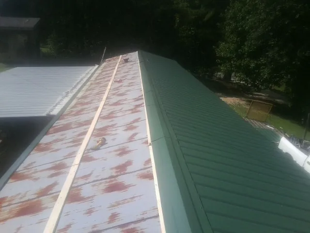 Old rusted panels beside newly installed green metal roofing — Wind Damage Roof Repair by Roofing Brothers in Kinston
