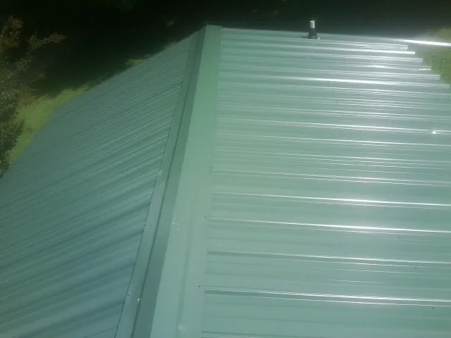 New green metal panels meeting at the ridge of a roof — Flat Roof Repair work by our crew in Kinston
