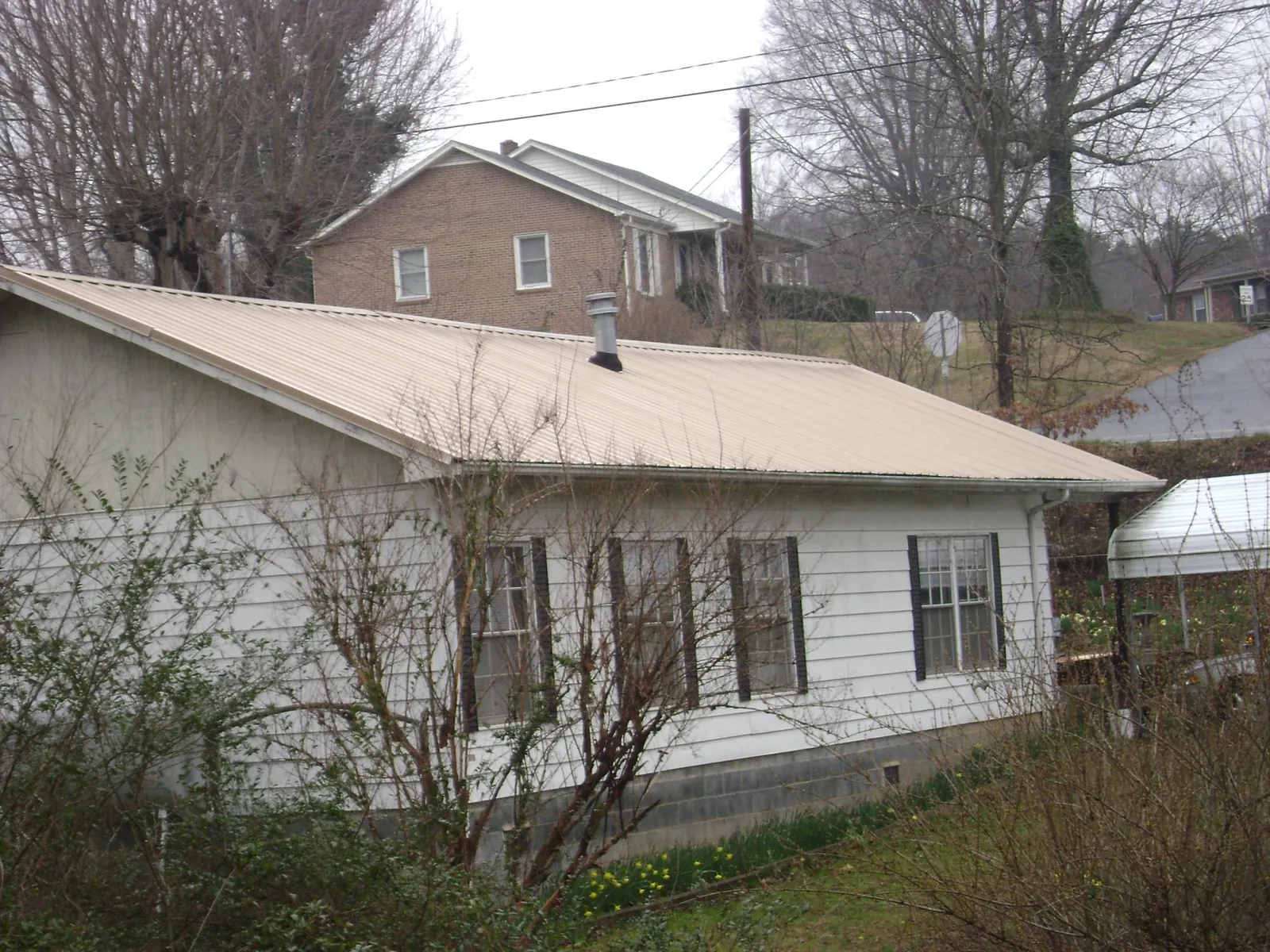 Tan metal roof on a white sided house set into a hillside — Commercial Roofing by Roofing Brothers in Kinston