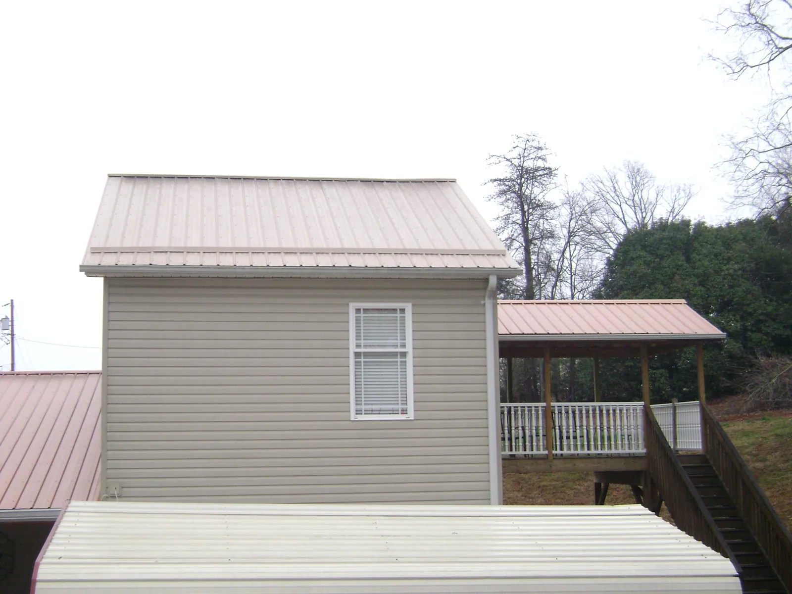 Tan metal roofs on a two story addition and attached porch, from a Roof Replacement job in Kinston